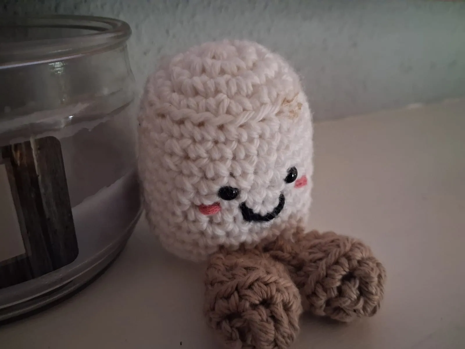 A cream crochet stuffed friend with a stitched smile, rosy cheeks and tan feet
