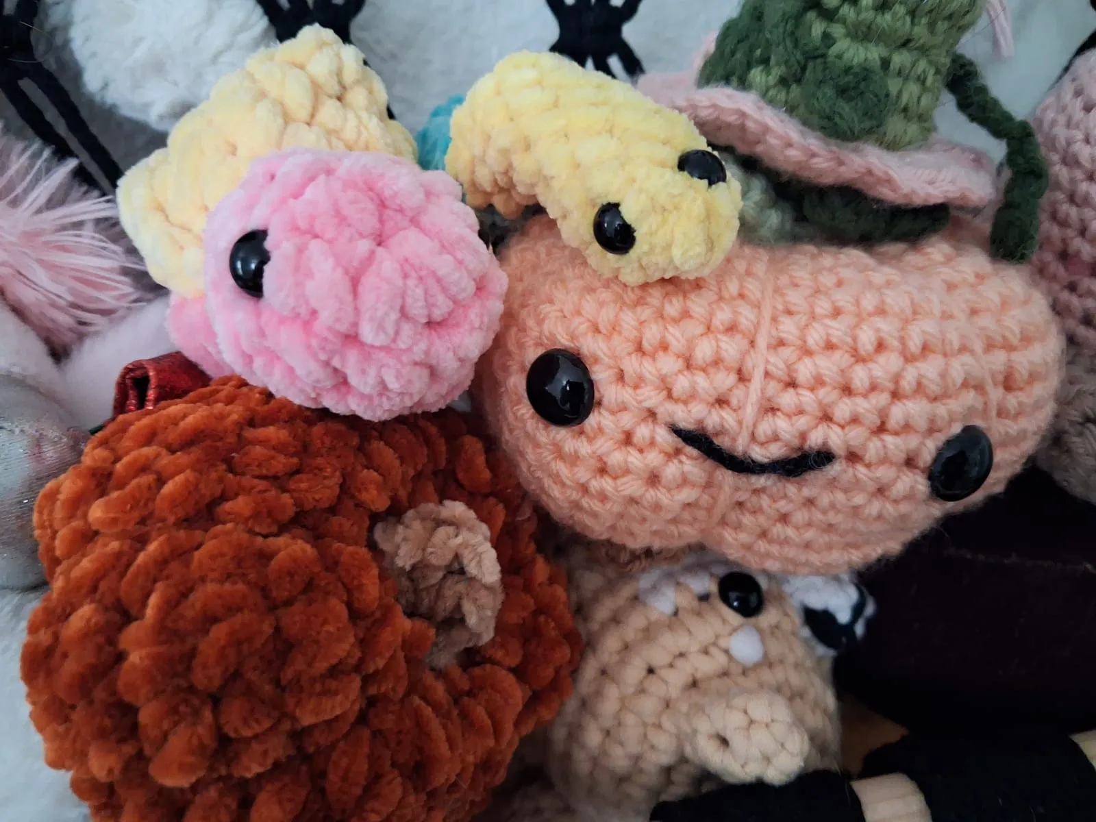 Close-up of a peach crochet friend with big eyes, a fluffy pink and yellow friend and a rust-colored friend