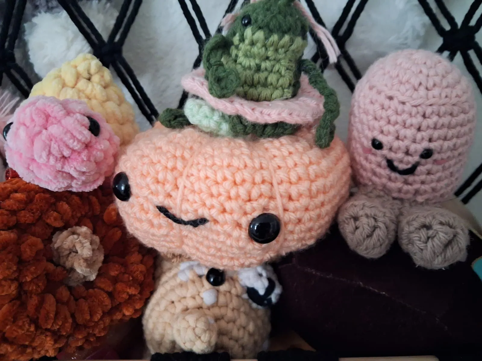 A group of crocheted stuffed animals in peach, pink, yellow, rust and green yarn